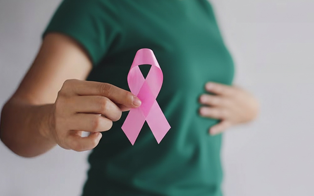 A woman holding a pink ribbon, symbolizing breast cancer awareness and the importance of early detection and support for breast cancer survivors.