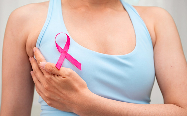 Close-up of woman wearing a pink ribbon for breast cancer awareness, holding her breast, symbolizing support, early detection, and advocacy for triple-negative breast cancer